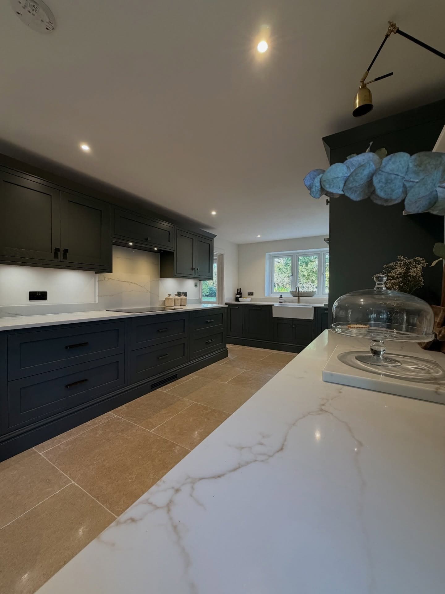 Kitchen island with veined quartz worktop, limestone floor and green in-frame cabinetry
