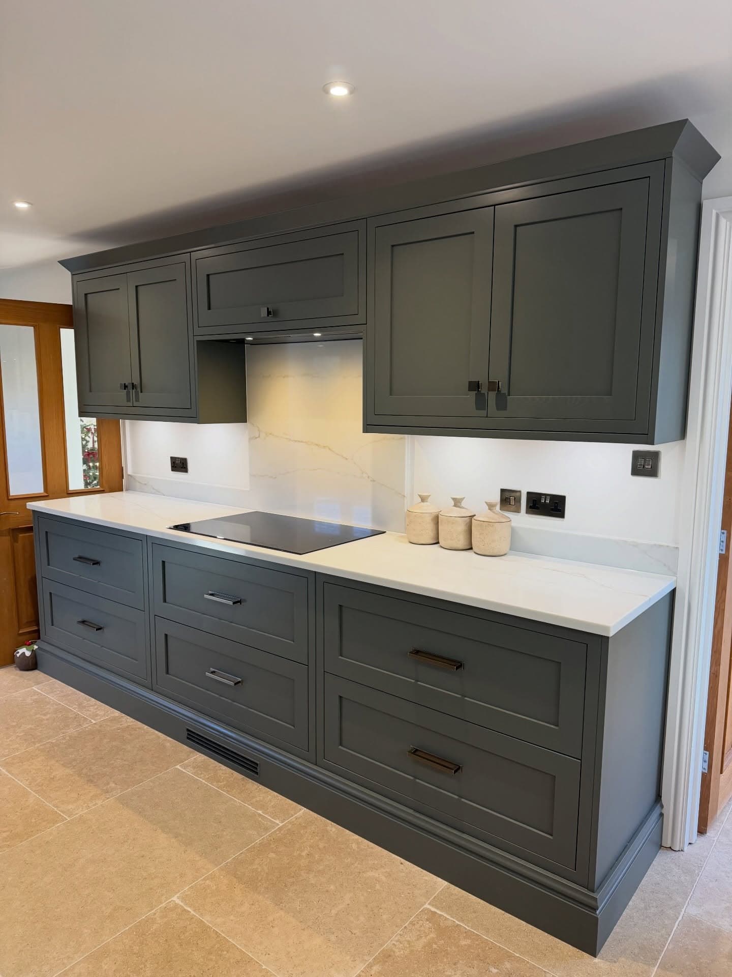 Green painted in-frame Howdens kitchen with a flush induction hob, quartz worktops and limestone floor