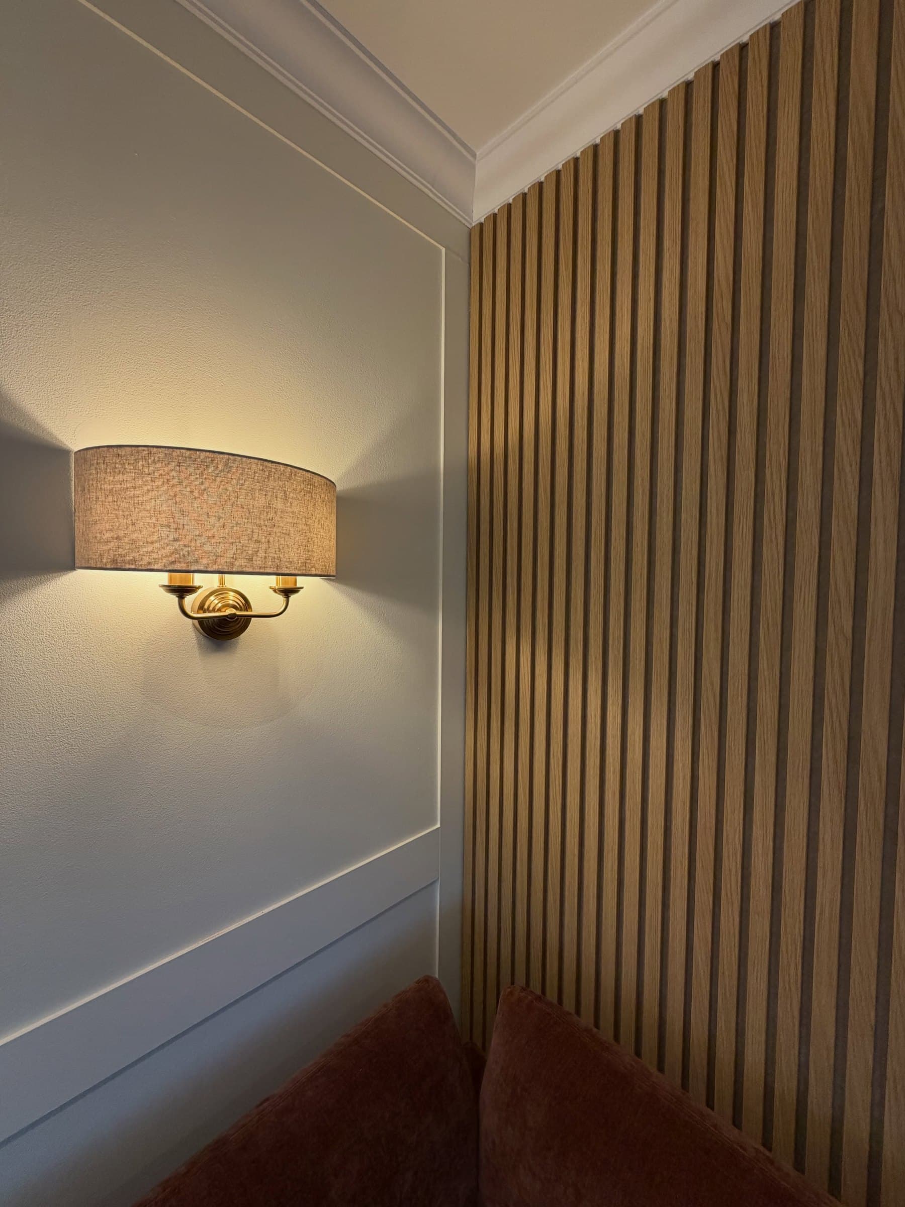 Shaker wall panelling meeting an oak slat feature wall, lit by a brass wall light